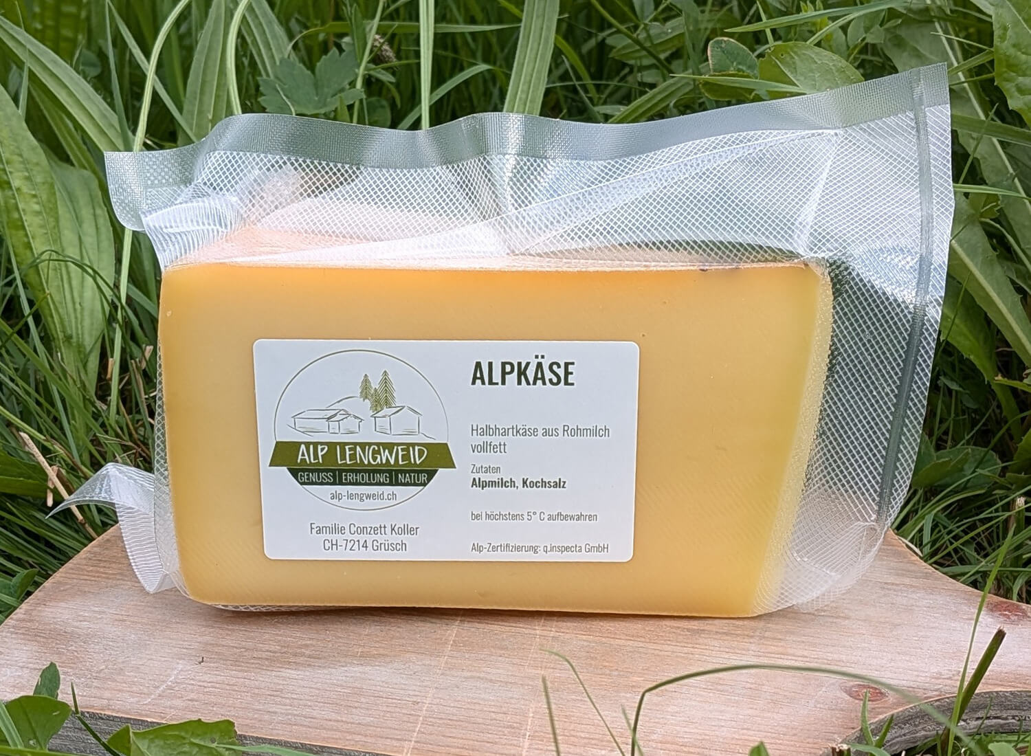 Alpkäse eingepackt auf Holzbrett im Gras